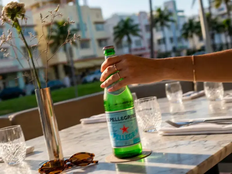 Hand holding a bottle of S.Pellegrino on a Miami restaurant terrace.