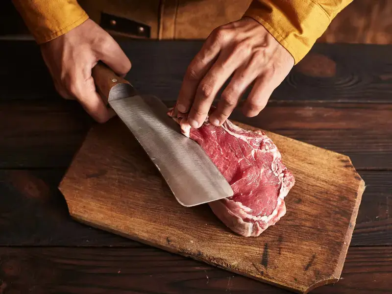 A butcher cutting a slab of lamb with a butcher's knife