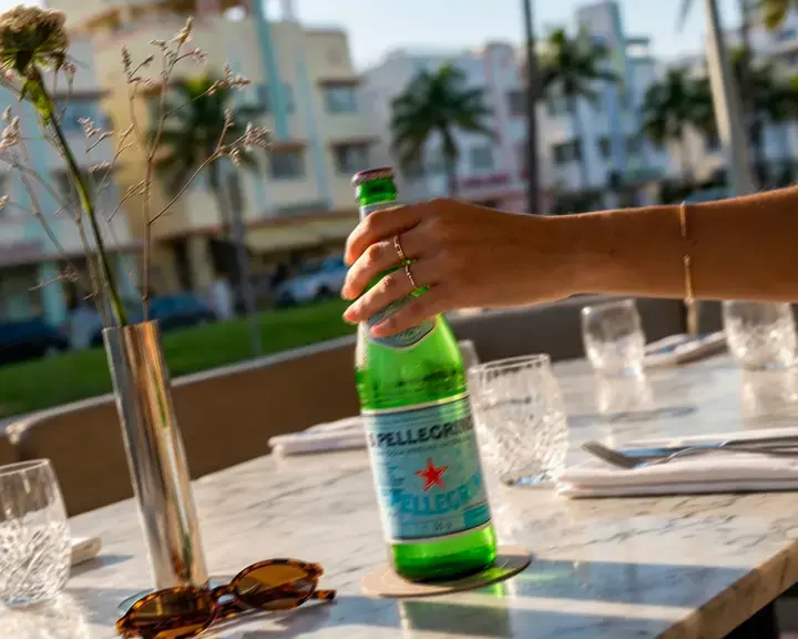 Hand holding a bottle of S.Pellegrino on a Miami restaurant terrace.